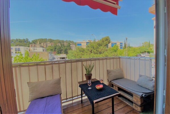 A balcony with a wooden table, two cushioned seating areas, a potted plant, and a bowl of snacks. - Very nice T4 +terrace, near town center, free parking (Aix-en-Provence)