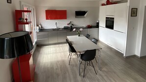 Eine moderne Küche mit weißen Schränken, einem Esstisch mit Stühlen und einer roten Akzentwand.