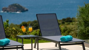 A terrace with two lounge chairs, a table with two drinks, and a view of the sea and a small island.