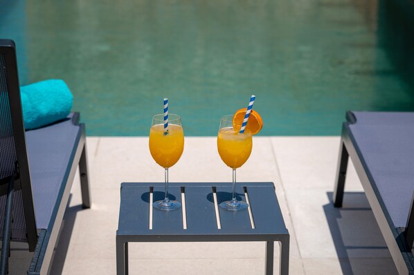 Una mesa junto a la piscina con dos vasos de zumo de naranja y una toalla.