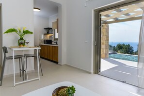 A modern kitchen with a view of the sea, a dining area with a table and chairs, and a large sliding glass door leading to an outdoor pool area.