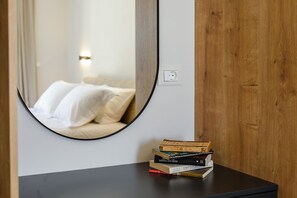 Una habitación con un espejo redondo en la pared, una mesita de noche con una pila de libros y un enchufe a la vista.