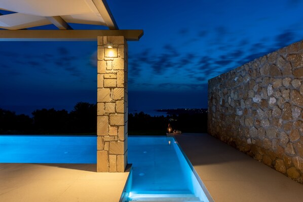 A swimming pool with a stone wall and a pergola structure.