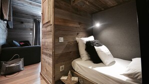 A compact room with a bed, a small seating area, and wooden walls. - Chalet Ankaa Collection Greniers d'Alpages (BOLQUÈRE FONT-ROMEU)
