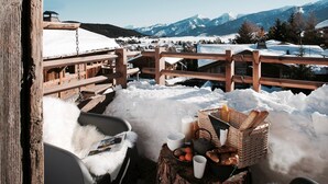 A wooden deck with a rustic bench, a wicker basket with bread, and a bottle of milk on a tree stump. - Chalet Ankaa Collection Greniers d'Alpages (BOLQUÈRE FONT-ROMEU)