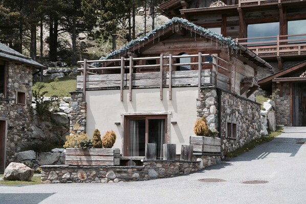Un refugio montañoso rústico con fachada de piedra, balcón de madera y entrada de piedra.