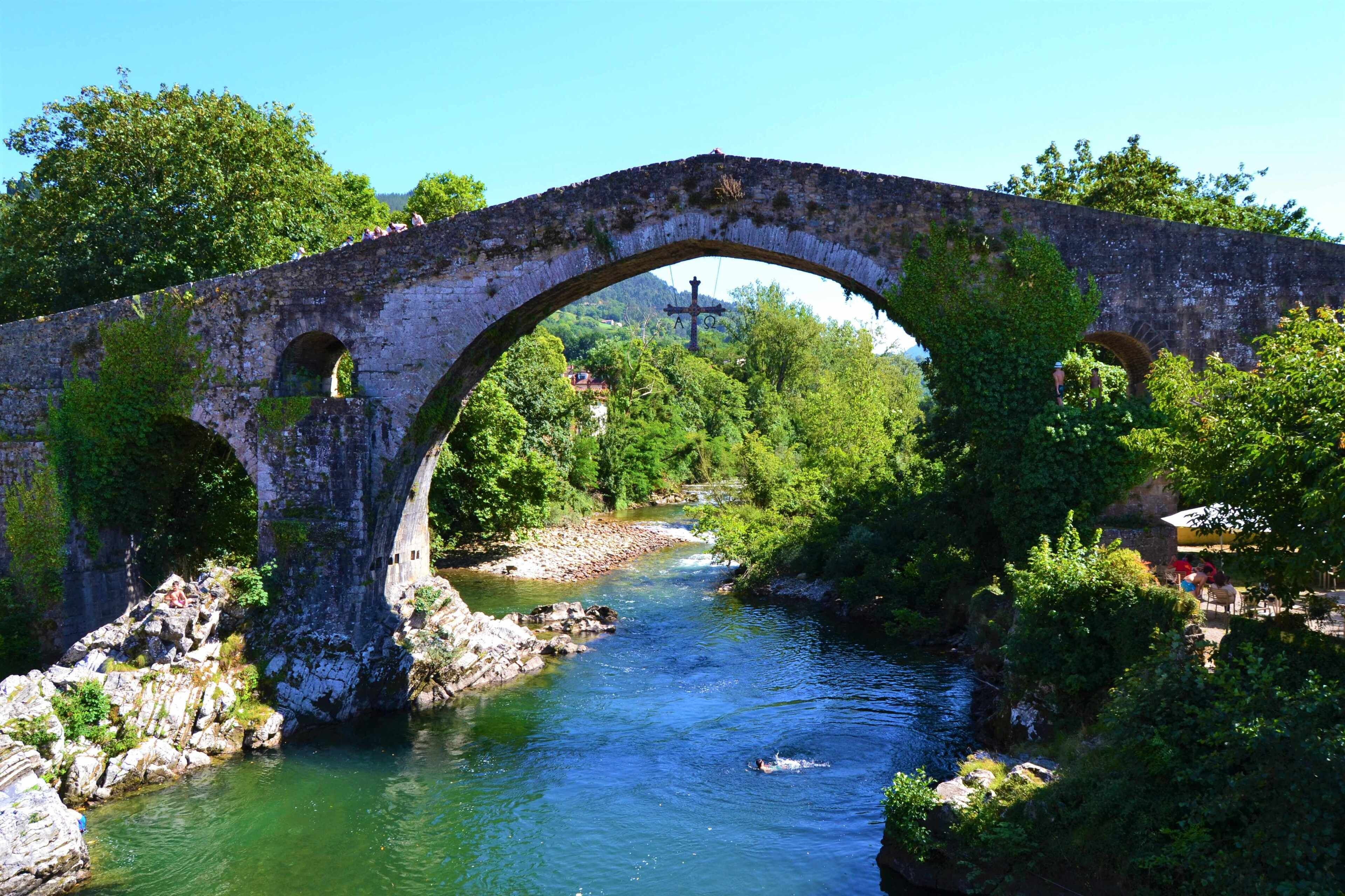 Uma ponte de pedra antiga sobre um rio, com vegetação exuberante em ambos os lados.
