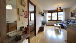 Un salon moderne avec un canapé, une table basse, un téléviseur et une cheminée. Un miroir est accroché au mur et une petite plante est posée sur la table.
