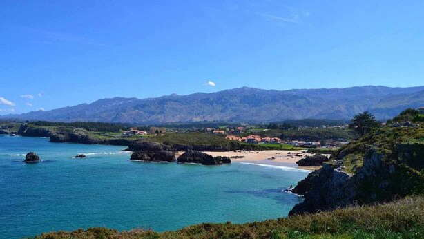 Un paysage côtier avec une plage, des affleurements rocheux et des montagnes en arrière-plan.