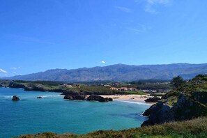 Un paisaje costero con una playa, afloramientos rocosos y montañas al fondo.