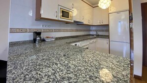 Une cuisine dotée de plans de travail en granit, d’armoires blanches, d’un four à micro-ondes, d’une machine à café et d’un réfrigérateur.