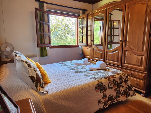 Un dormitorio con una cama, un armario de madera, una ventana con cortinas y un ventilador.