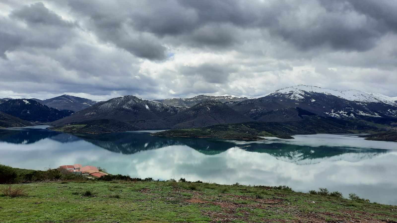 A mountainous landscape with a lake and a small building in the foreground.