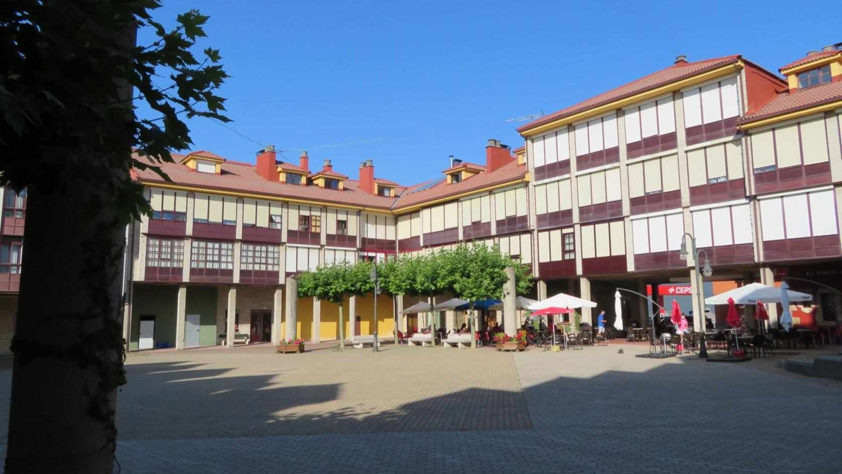 A courtyard with a building featuring a symmetrical facade, multiple windows, and a red-tiled roof. There are outdoor seating areas with umbrellas and tables.