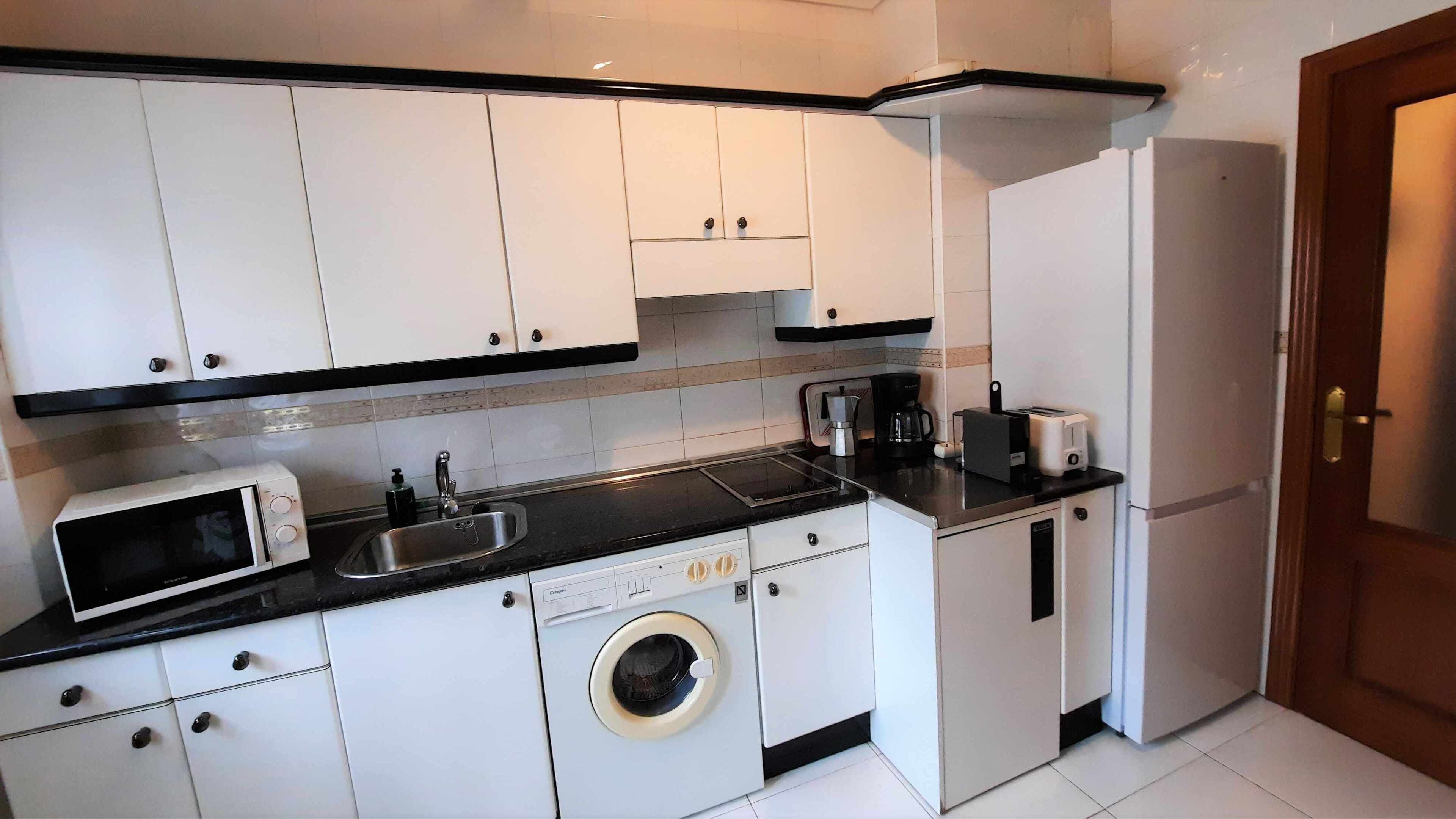 A compact kitchen with white cabinets, a microwave, a sink, a coffee maker, a toaster, and a washing machine.