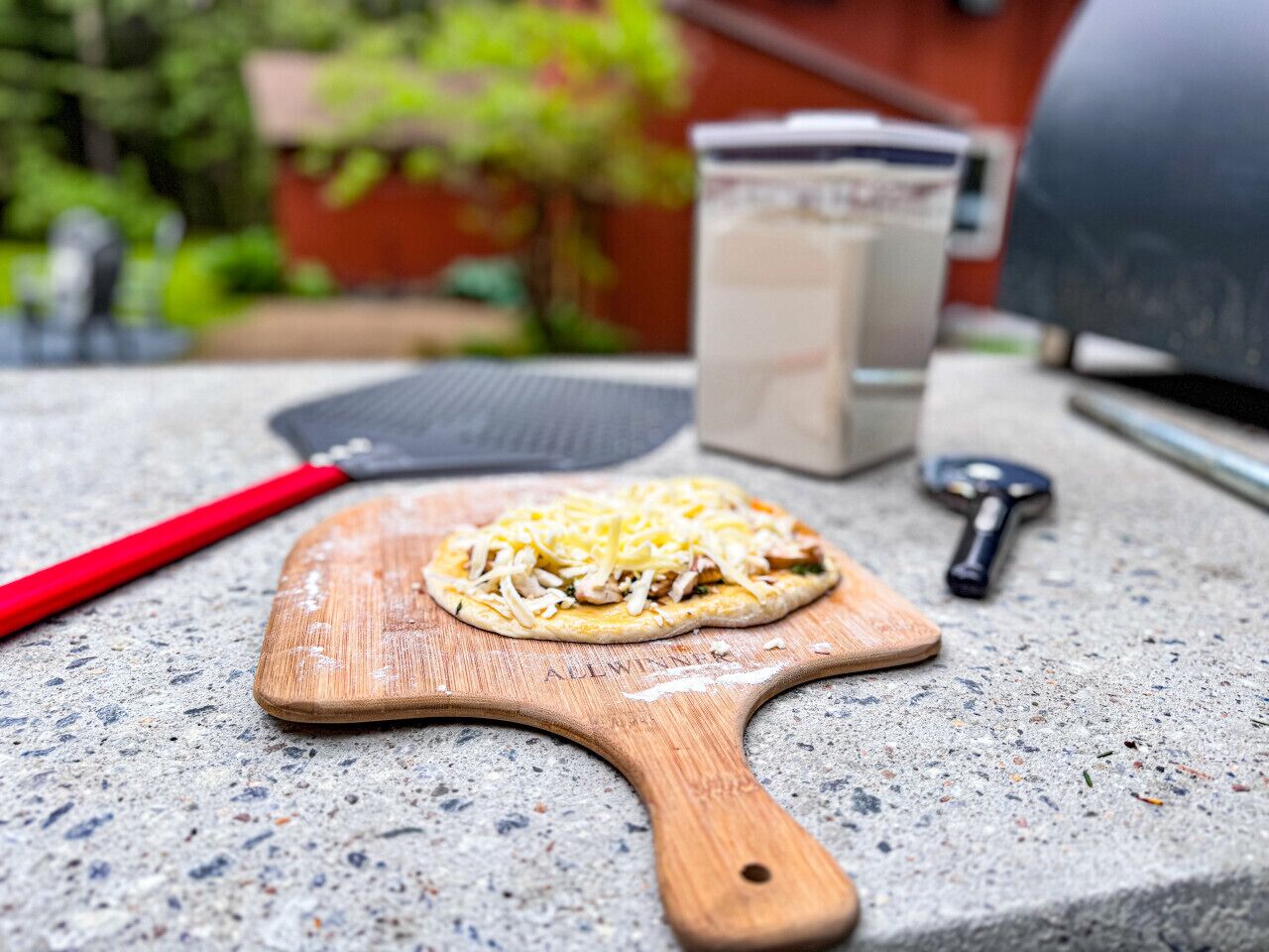 A pizza on a wooden board with a red-handled spatula beside it.