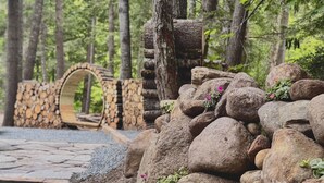 Un pont de pierre rustique, une arche en bois et un amas de gros rochers parsemés de petites plantes.