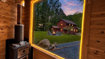 A wooden cabin interior with a sauna, a window view of a house, and a stone fireplace.