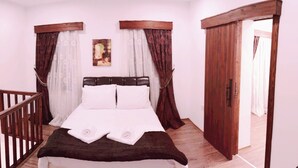 Une chambre à coucher avec un lit, une tête de lit en bois, des rideaux blancs et une porte en bois.