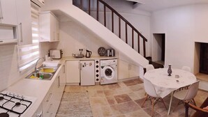 Une cuisine compacte équipée d’une cuisinière à gaz, d’un lave-linge et d’une table à manger avec des chaises.
