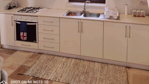 Une cuisine moderne avec des meubles blancs, une cuisinière à gaz, un four encastré et une fenêtre équipée de stores.