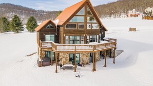 Une grande cabane en bois, avec des fondations en pierre, un balcon et un paysage enneigé.