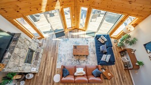 Un vaste espace de vie agrémenté d’une cheminée en pierre, d’un plafond en bois et d’une grande verrière.
