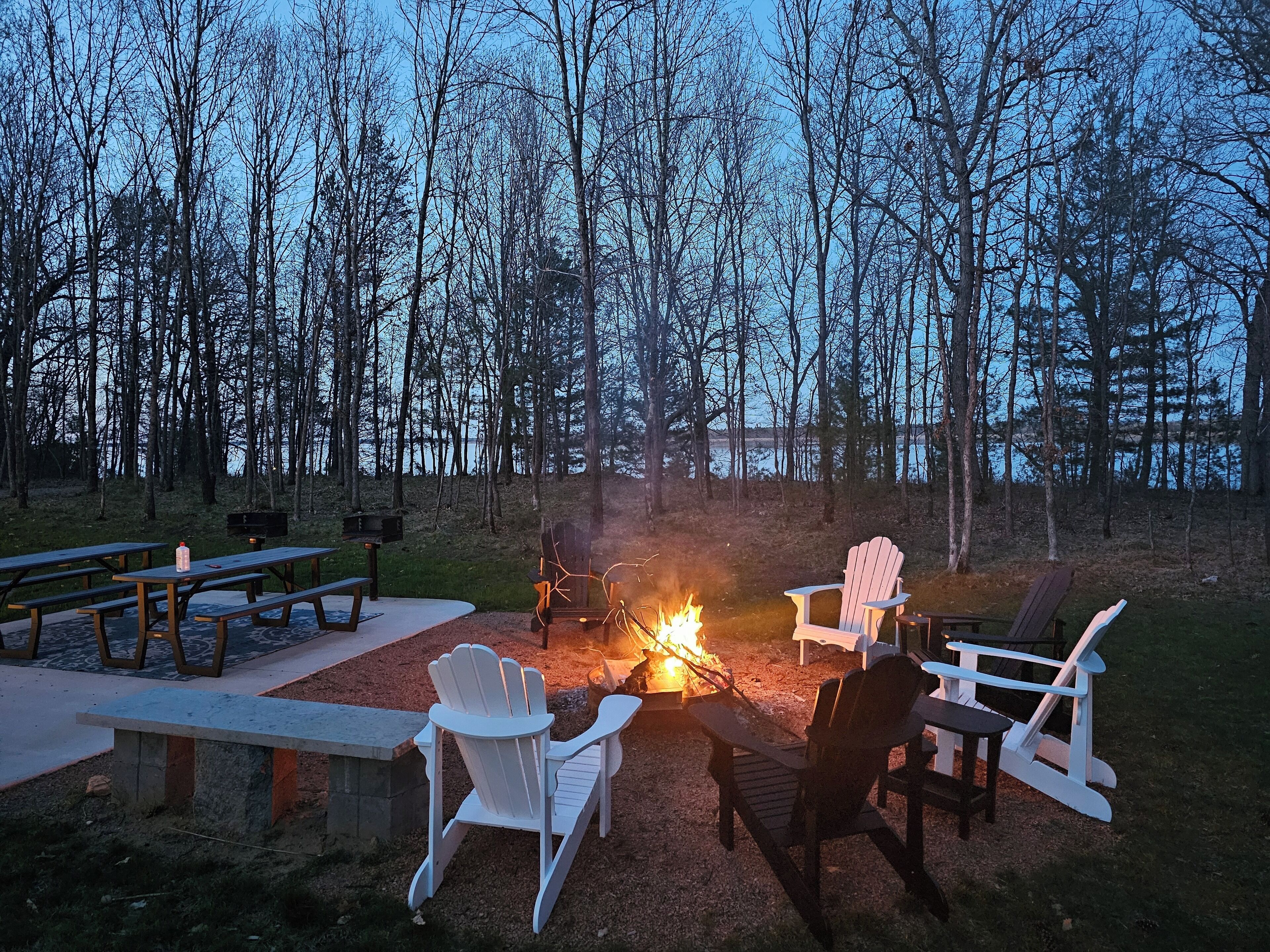 An outdoor seating area with a fire pit, picnic tables, and Adirondack chairs.