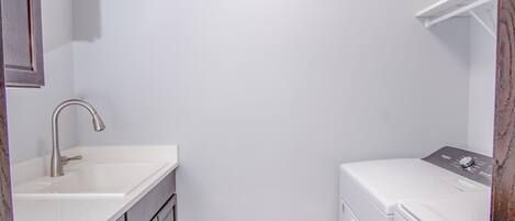 A small, clean laundry room with a white washing machine and a sink.