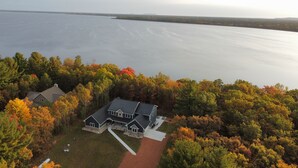 Una vista aerea di una casa circondata da fogliame autunnale e un ampio specchio d'acqua.
