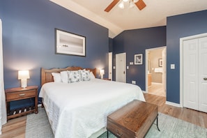 Une chambre à coucher avec un grand lit, des tables de chevet en bois, une commode et un ventilateur de plafond.