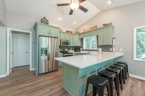 Une cuisine avec des meubles de couleur turquoise, un réfrigérateur en acier inoxydable, un four à micro-ondes et un grand îlot central doté de tabourets de bar.