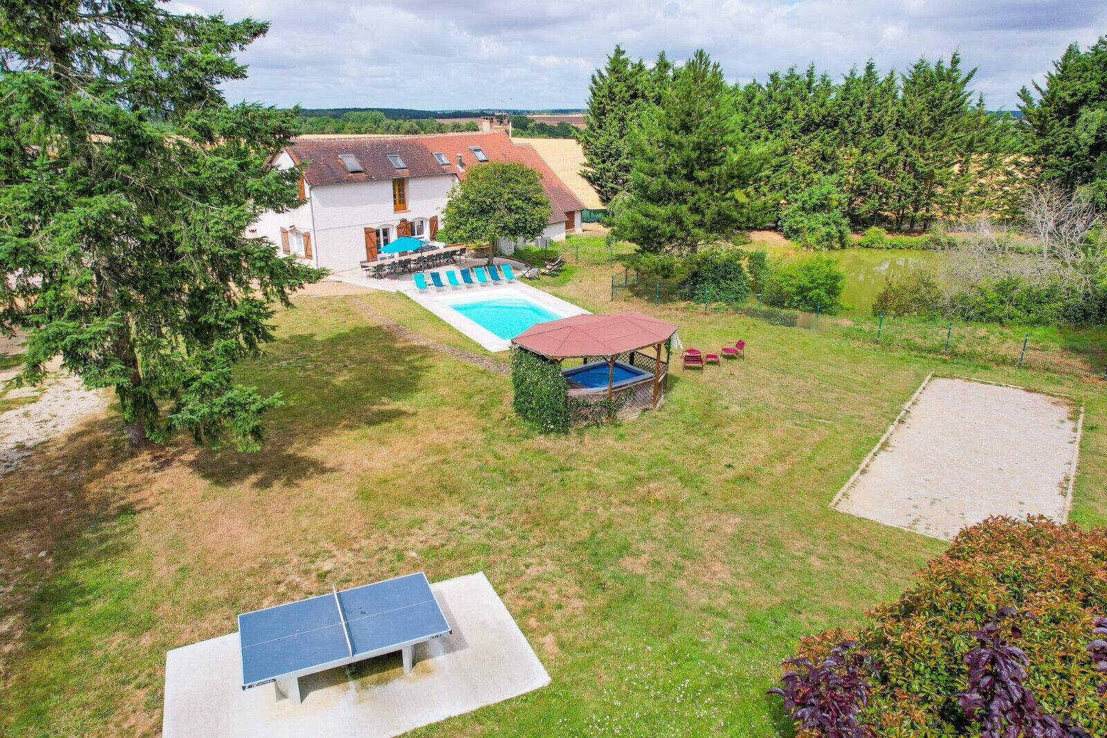 A backyard with a swimming pool, a ping pong table, and a covered seating area.