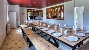 Een lange eettafel gedekt met witte borden, wijnglazen en bestek, met een keuken op de achtergrond.