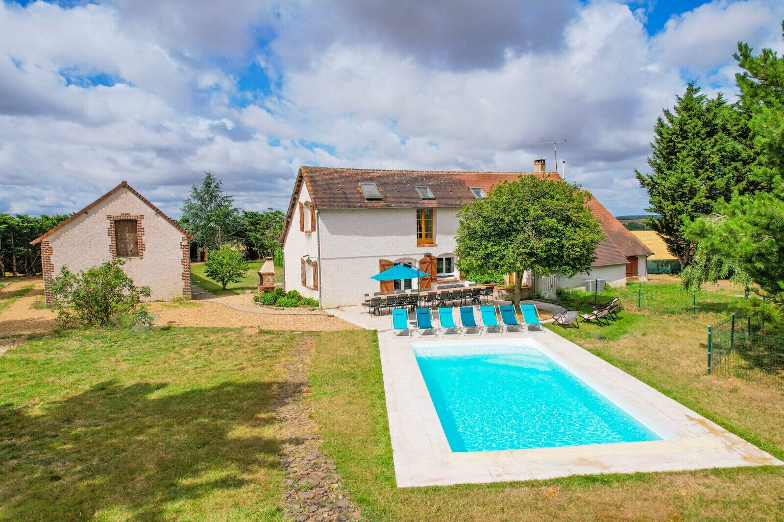 Una casa con piscina, un patio con sillas y un pequeño jardín.