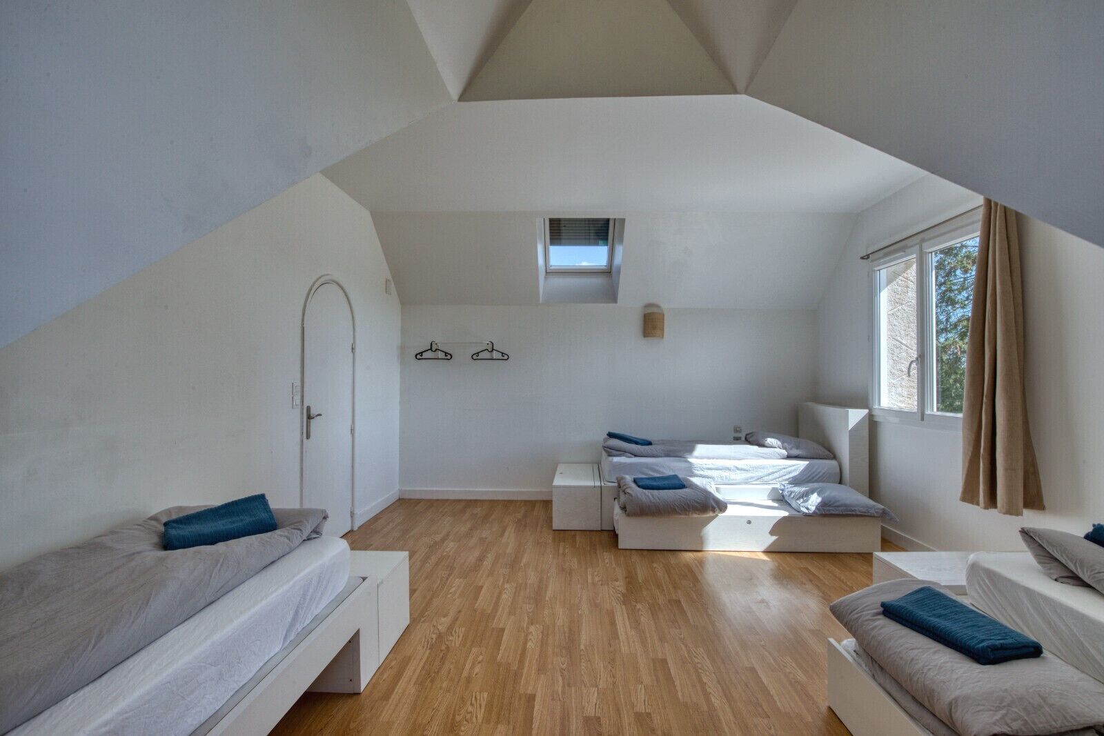 Camera da letto moderna e luminosa con soffitto spiovente, pavimento in legno e un'ampia finestra che offre luce naturale.