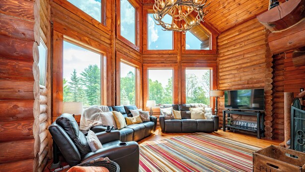 A log cabin interior with a large window, a fireplace, a television, and a sofa. - Dog Friendly Luxury Estate w/ Hot Tub & Dock (Oakland)