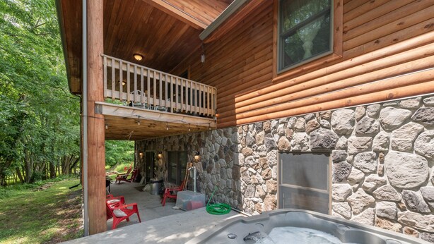 Une cabane en bois avec une façade en pierre, un jacuzzi et un balcon donnant sur un jardin.