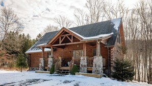 Une cabane en rondins avec un porche en pierre, une terrasse en bois et un toit recouvert de neige.