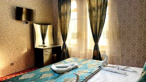 A hotel room with a bed, a TV mounted on the wall, a desk with drawers, and curtains on the windows. - Diva Hotel (Baku)
