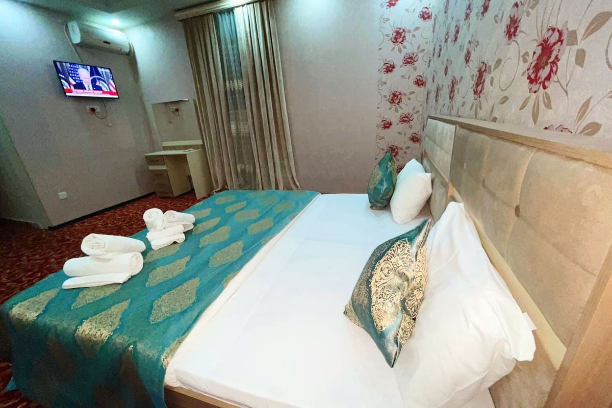 A hotel room with a bed, a TV on the wall, and a desk with a chair.