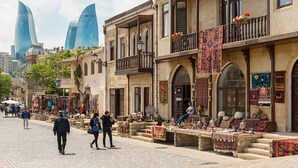 A street with traditional buildings, a market, and modern skyscrapers in the background. - Diva Hotel (Baku)