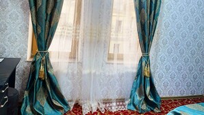 A room with patterned wallpaper, a bed with a red and gold bedspread, and teal curtains with gold detailing. - Diva Hotel (Baku)