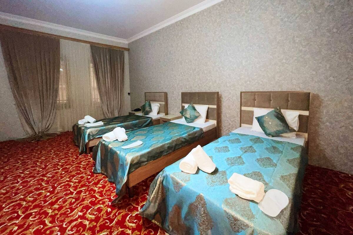 A hotel room with three beds, each with a headboard, and a red patterned carpet.