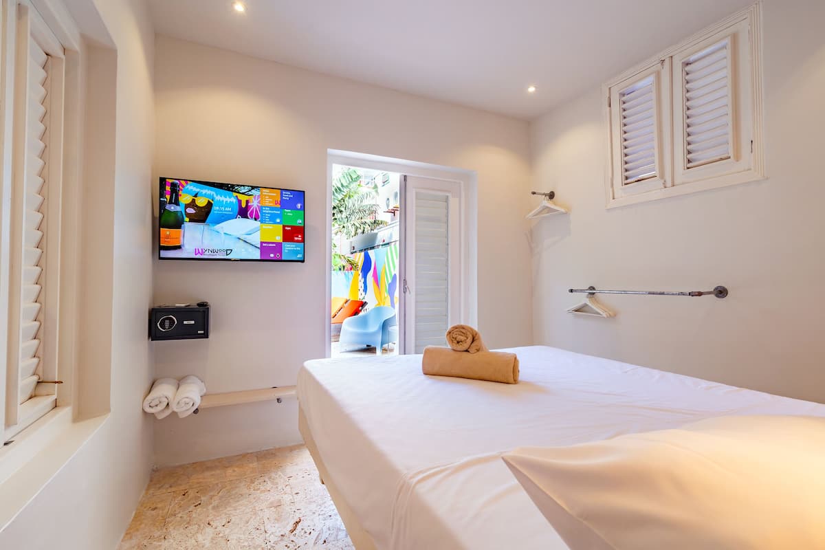 A hotel room with a bed, a TV mounted on the wall, a window with shutters, and a towel rack.