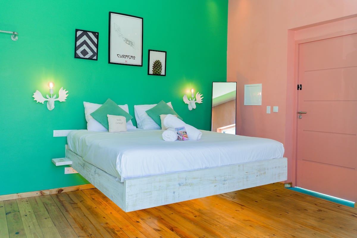 A bedroom with a bed, green walls, a wooden floor, and a pink door.