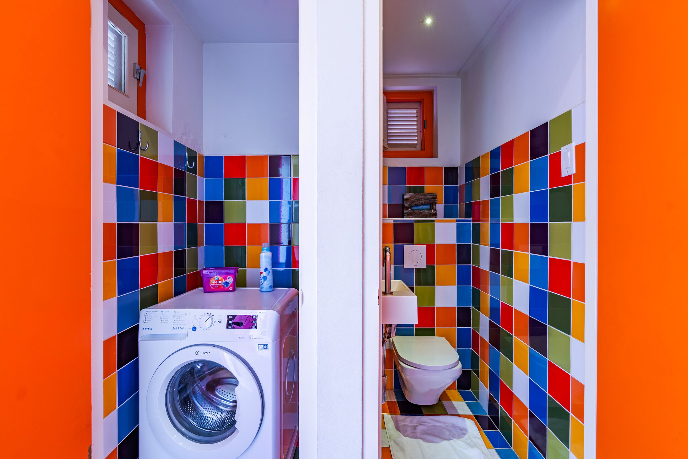 Un baño pequeño con baldosas de colores, lavadora e inodoro.