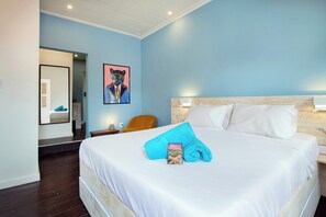 A hotel room with a large bed, a wooden headboard, a nightstand with a lamp, a framed artwork on the wall, and a blue towel on the bed. - Wynwood Boutique Hotel (Willemstad)