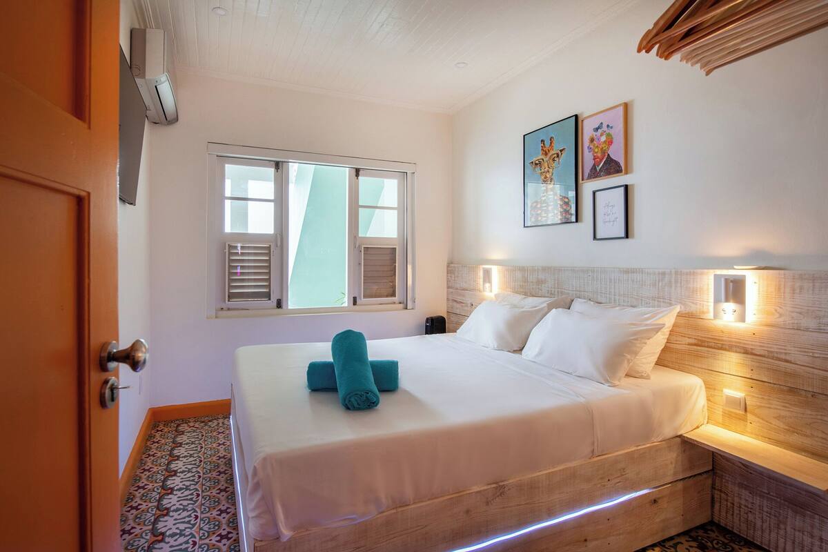 A hotel room with a bed, a window, and a wall-mounted light fixture.