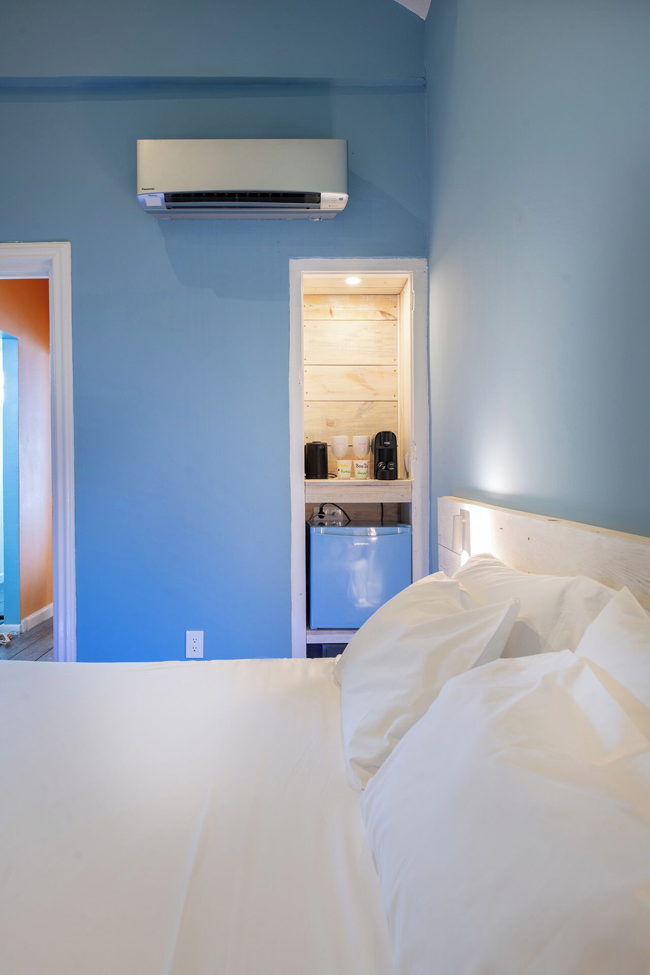 A hotel room with a bed, a kitchenette with a coffee maker, and an air conditioning unit.
